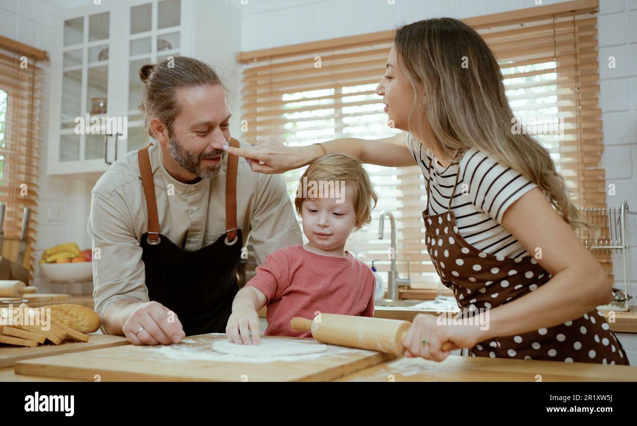 Padre e madre insegnano al bambino impastare sul banco della cucina a casa. I genitori e il bambino del ragazzo godono e divertimento cucinano insieme l'attività interna. Foto Stock