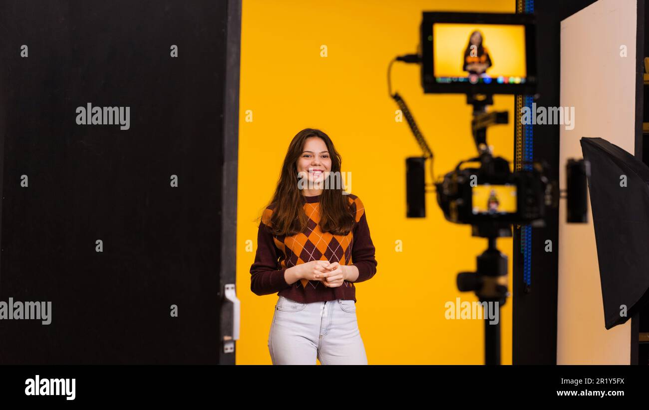 Vista di una fotocamera professionale con display esterno che riprende una giovane donna su sfondo giallo Foto Stock
