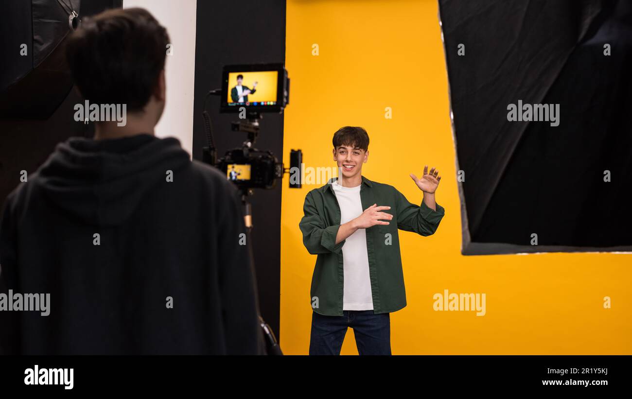 Vista di un fotografo professionista che scatta foto a un giovane utilizzando una fotocamera con display esterno, sfondo giallo Foto Stock