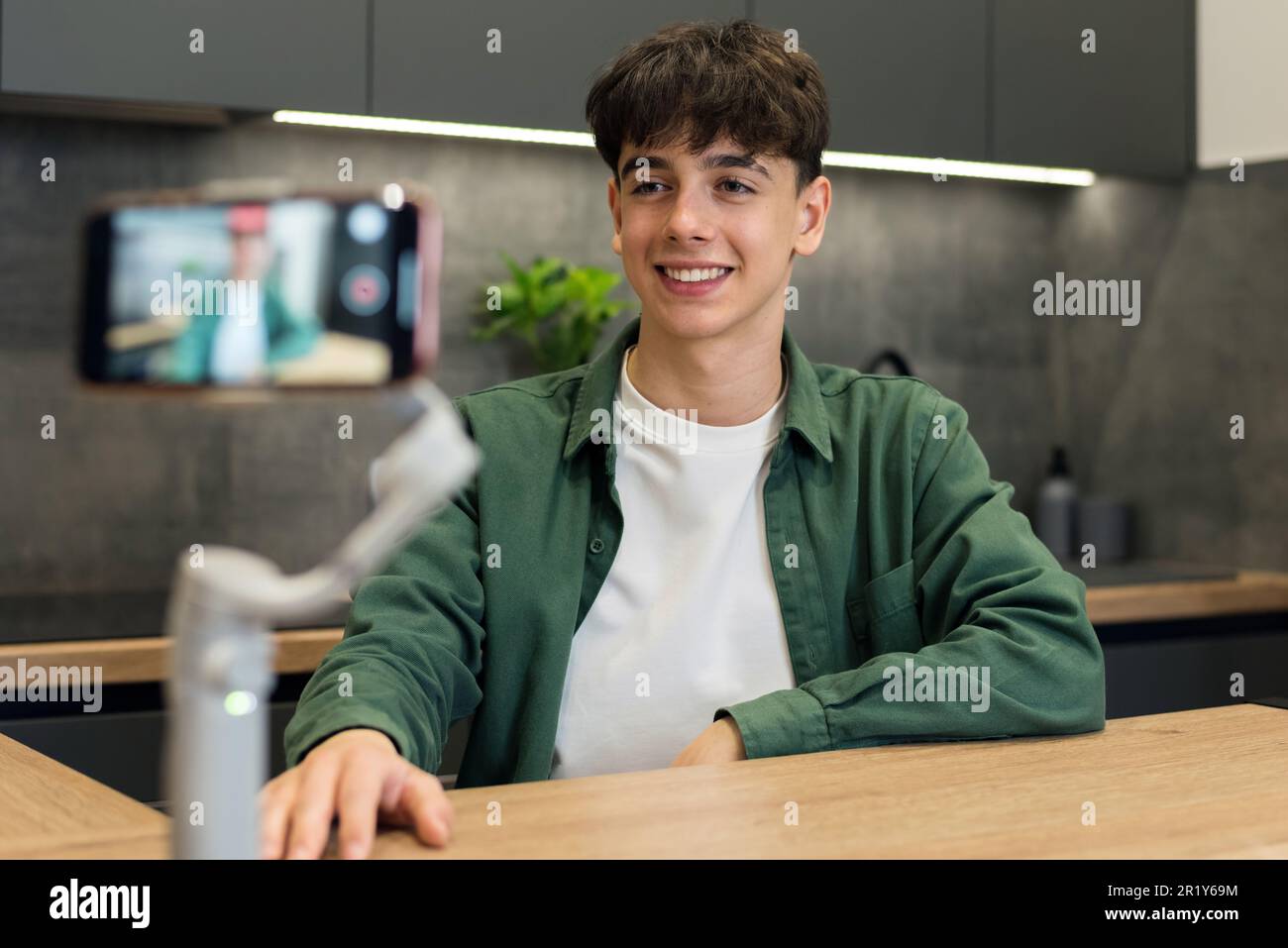 Giovane uomo sorridente blogger influencer sparare se stesso su uno smartphone su uno stabilizzatore in cucina Foto Stock