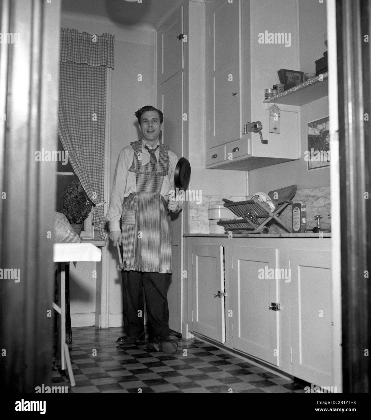 Uomo degli anni '1950s. Il ballerino svedese Mario Mengarelli in cucina guardando come preparato come ci si può aspettare da un maschio 1950s, indossando un grembiule, tenendo una padella padella guardare malriposto. Svezia 1952 Ref 1958 Foto Stock