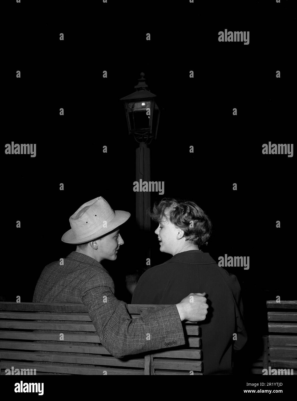 Negli anni '1950s. Una giovane coppia è seduta su una panchina e guarda af sta facendo un tentativo di mettere il suo braccio intorno a lei, facendolo passo dopo passo. Forse una prima data. Svezia 1953 Kristoffersson Ref 15K-21 Foto Stock