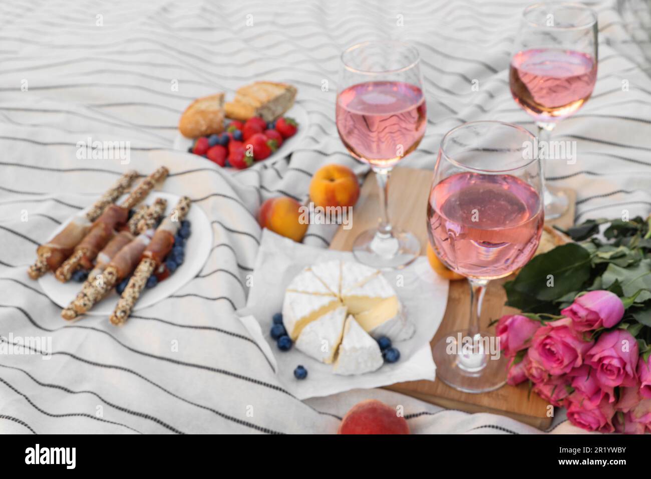 Bicchieri di delizioso vino rosa, fiori e cibo su coperta bianca da picnic Foto Stock