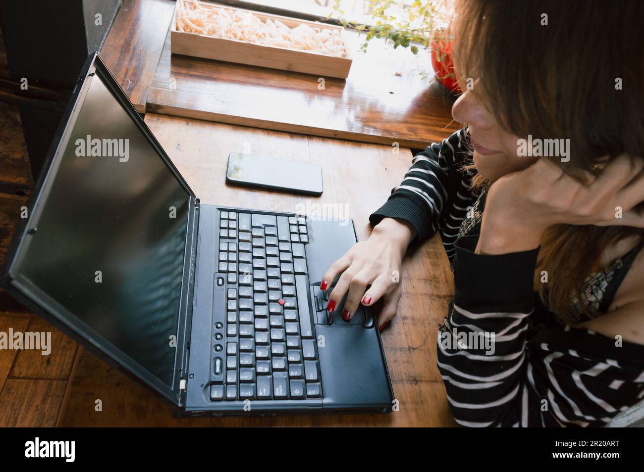 Profilo primo piano di una giovane donna transgender Latina di etnia argentina, utilizzando il suo laptop in un ristorante, navigando in internet, controllando le e-mail Foto Stock