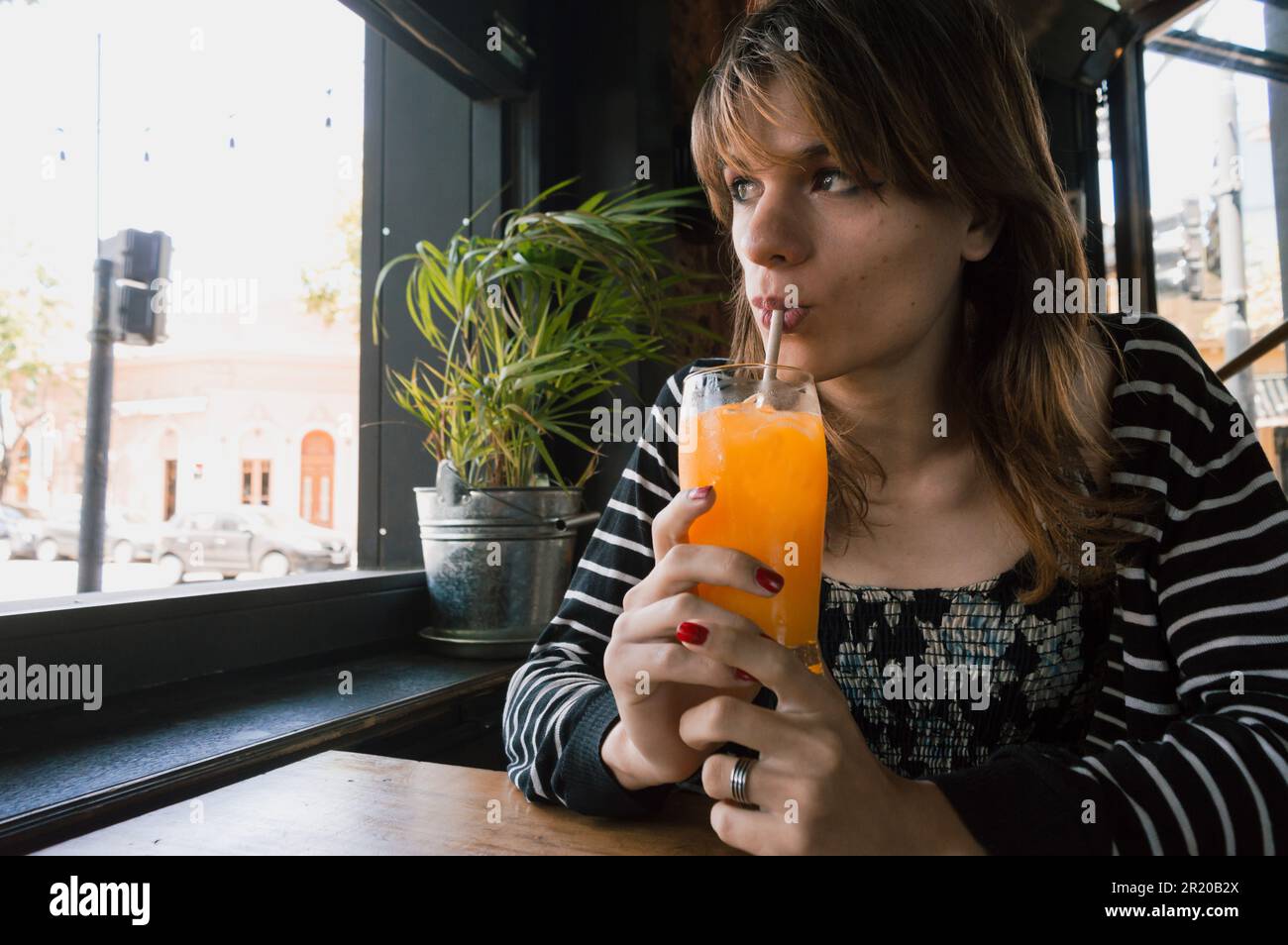ritratto di giovane latina ispanica di etnia argentina, seduta bevendo succo d'arancia in un ristorante, in attesa del suo partner. Foto Stock