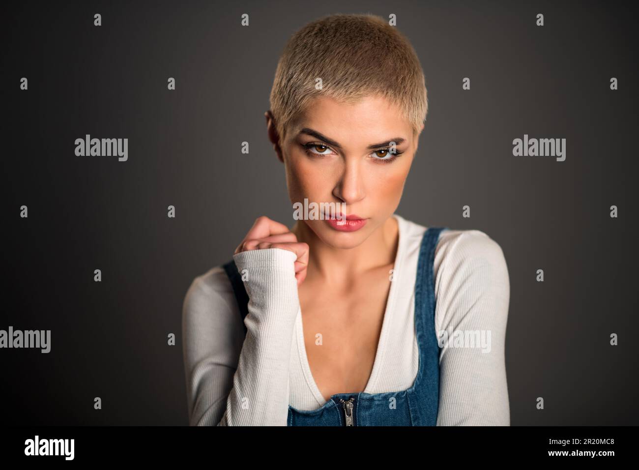 Ritratto di seria giovane donna con capelli corti biondi guardando la macchina fotografica contro il backgroundaq grigio Foto Stock