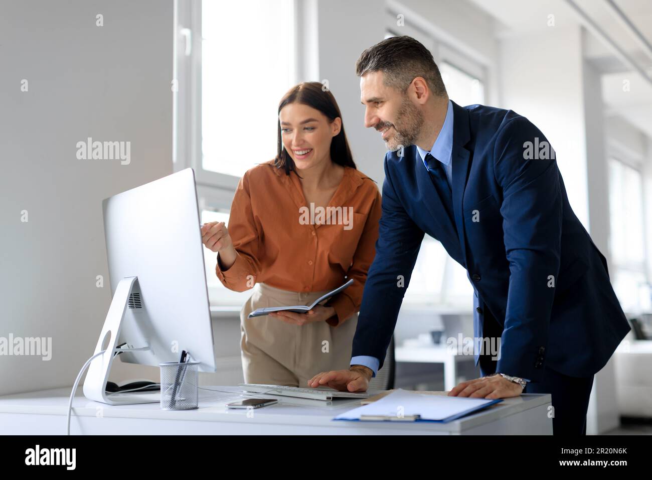 Felice giovane assistente signora e il suo capo lavorando insieme, utilizzando un computer moderno in ufficio Foto Stock