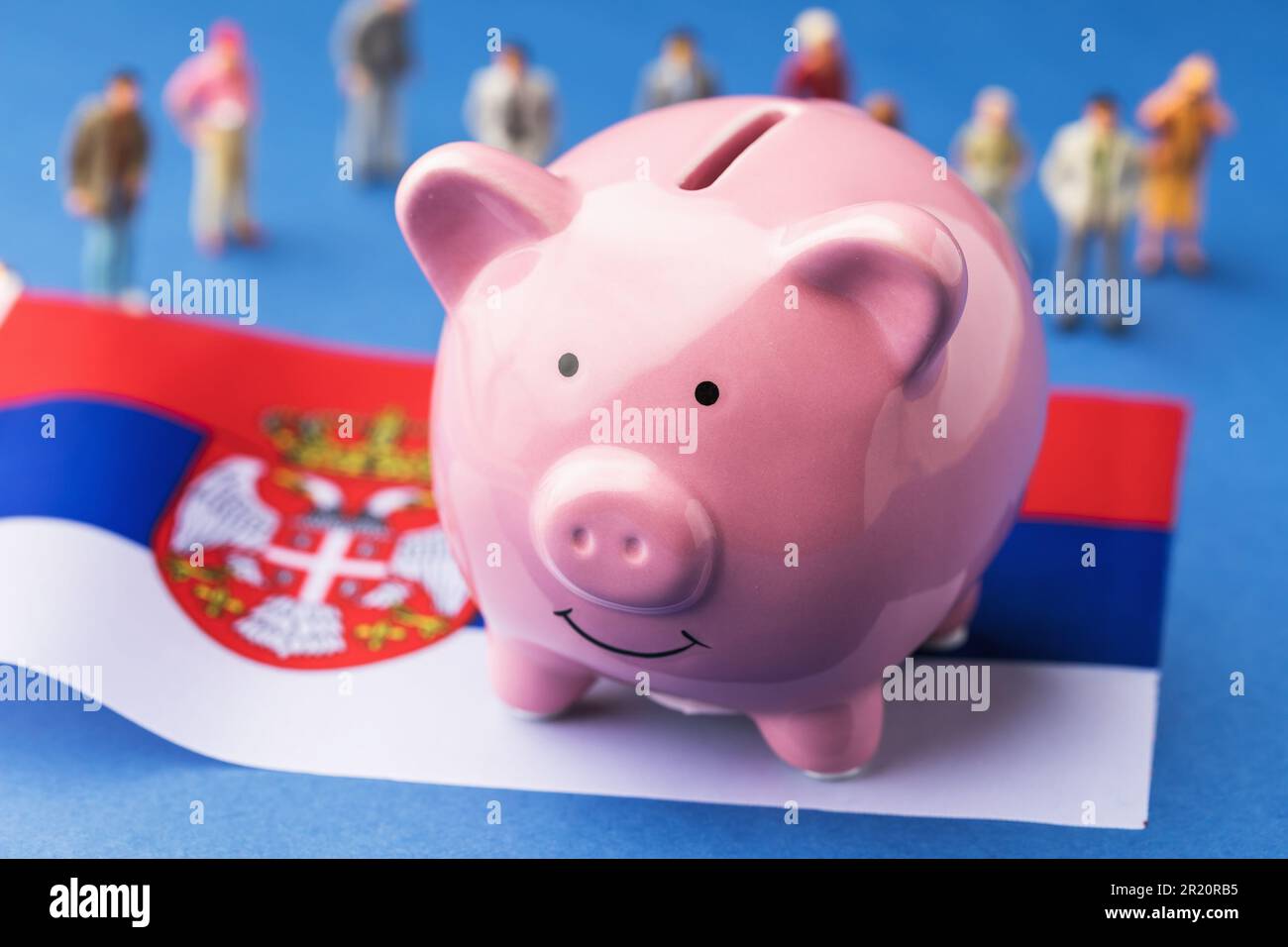 Banca di maialino, bandiera serba e giocattoli di plastica su sfondo colorato, un concetto sul tema del reddito della popolazione serba Foto Stock