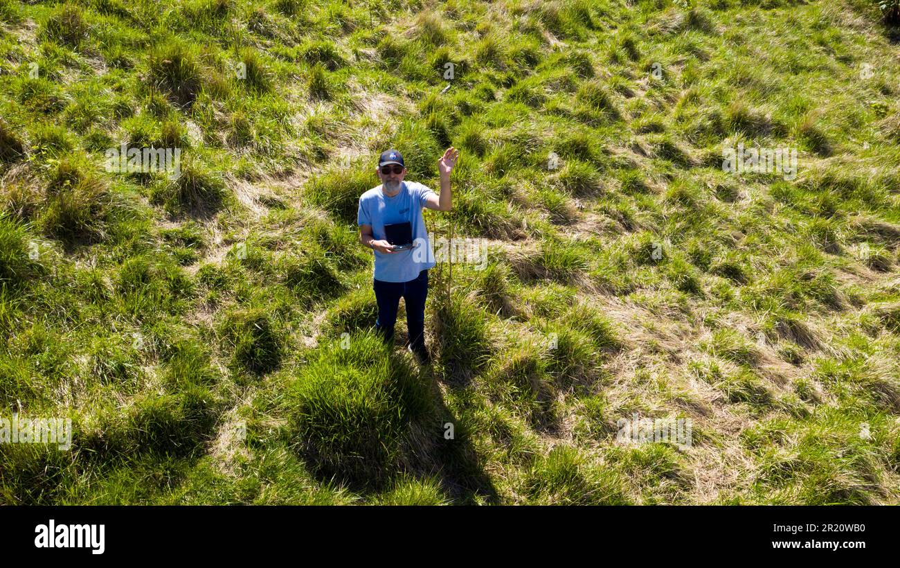 Pilota del drone, sorridendo e ondeggiando al drone, volando appena sopra la sua testa, sul Monte Coxhill, Kearsney, Kent Foto Stock