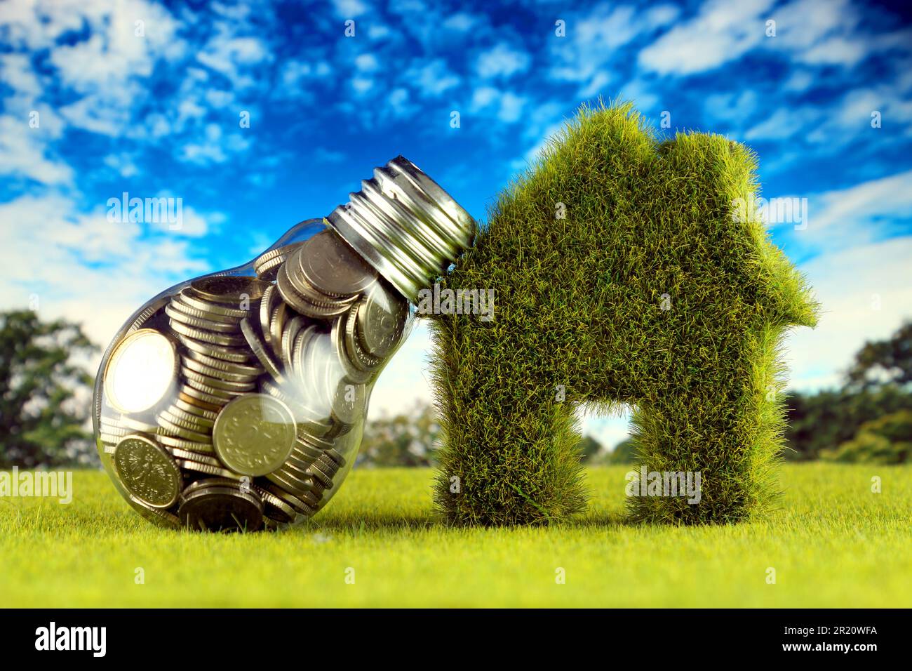 Monete all'interno della lampadina e casa in miniatura con erba. Eco-verde energia rinnovabile concetto. I prezzi dell'elettricità, il risparmio energetico in famiglia. Foto Stock