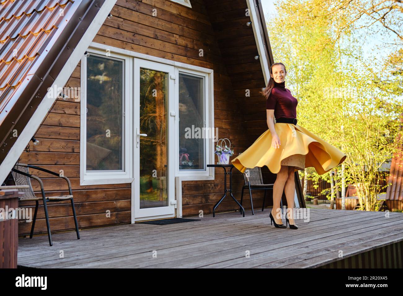 Una donna con gambe perfette in scarpe con tacco alto e gonna gialla gira intorno su una terrazza di legno Foto Stock
