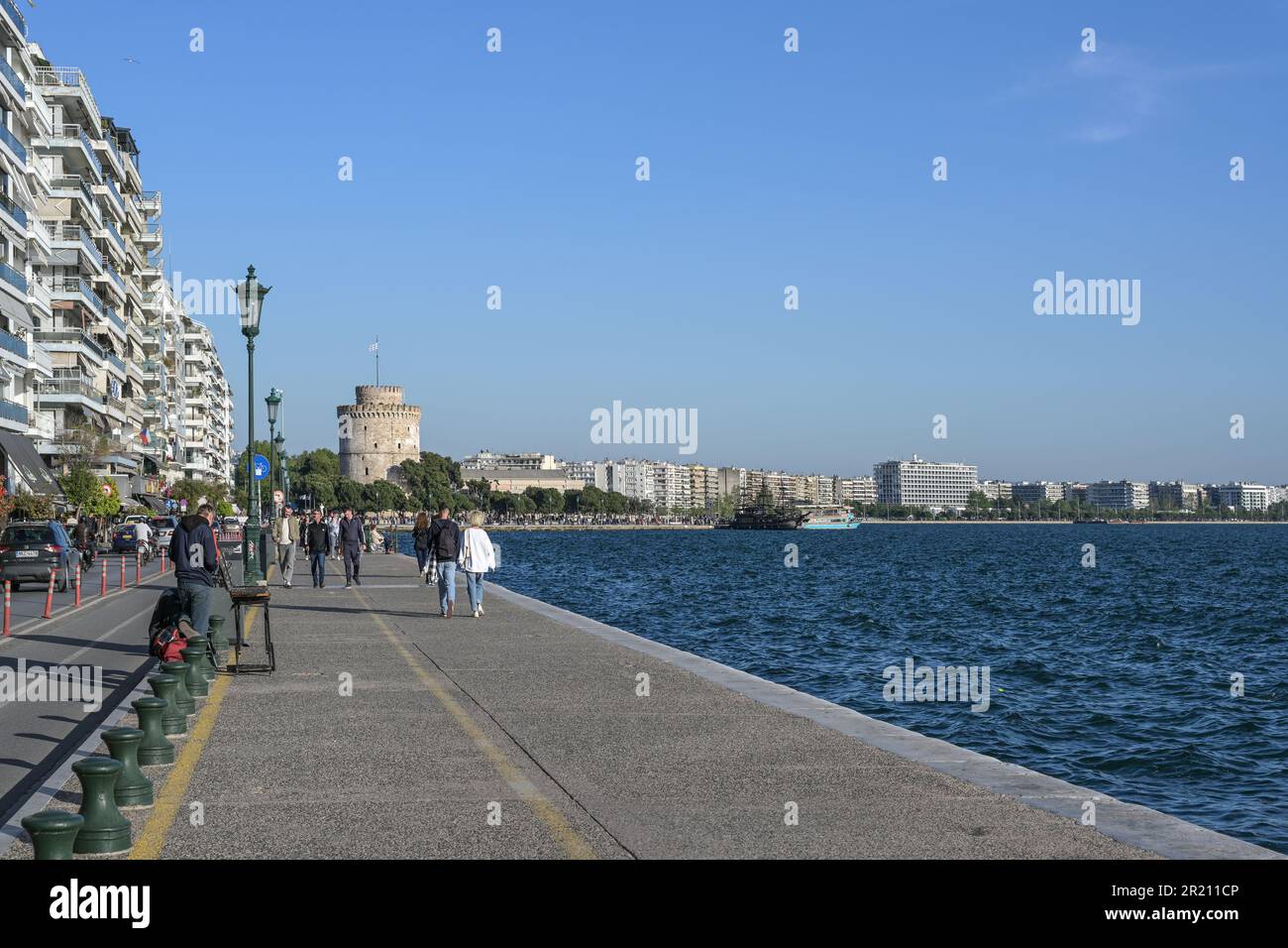 Salonicco, Grecia, 28 aprile 2023: Passeggiata sul mare nel Mar Mediterraneo con persone a piedi che conducono alla Torre Bianca, famoso punto di riferimento e. Foto Stock