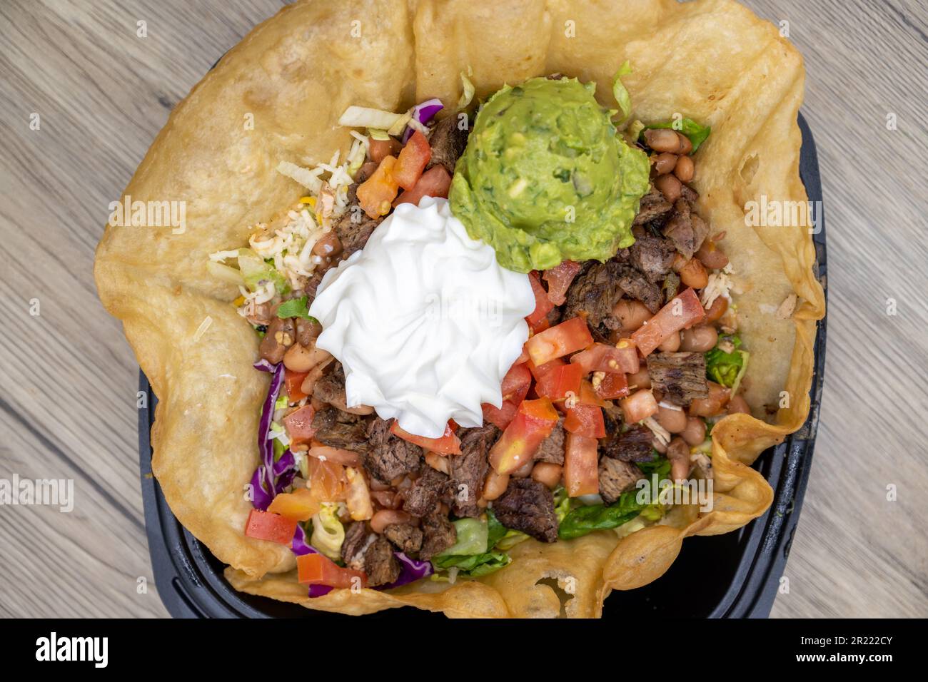 La vista dall'alto del guscio croccante della tostada contiene questa generosa insalata di fajita taco con grandi cucchiai di panna acida e guacamole in cima. Foto Stock