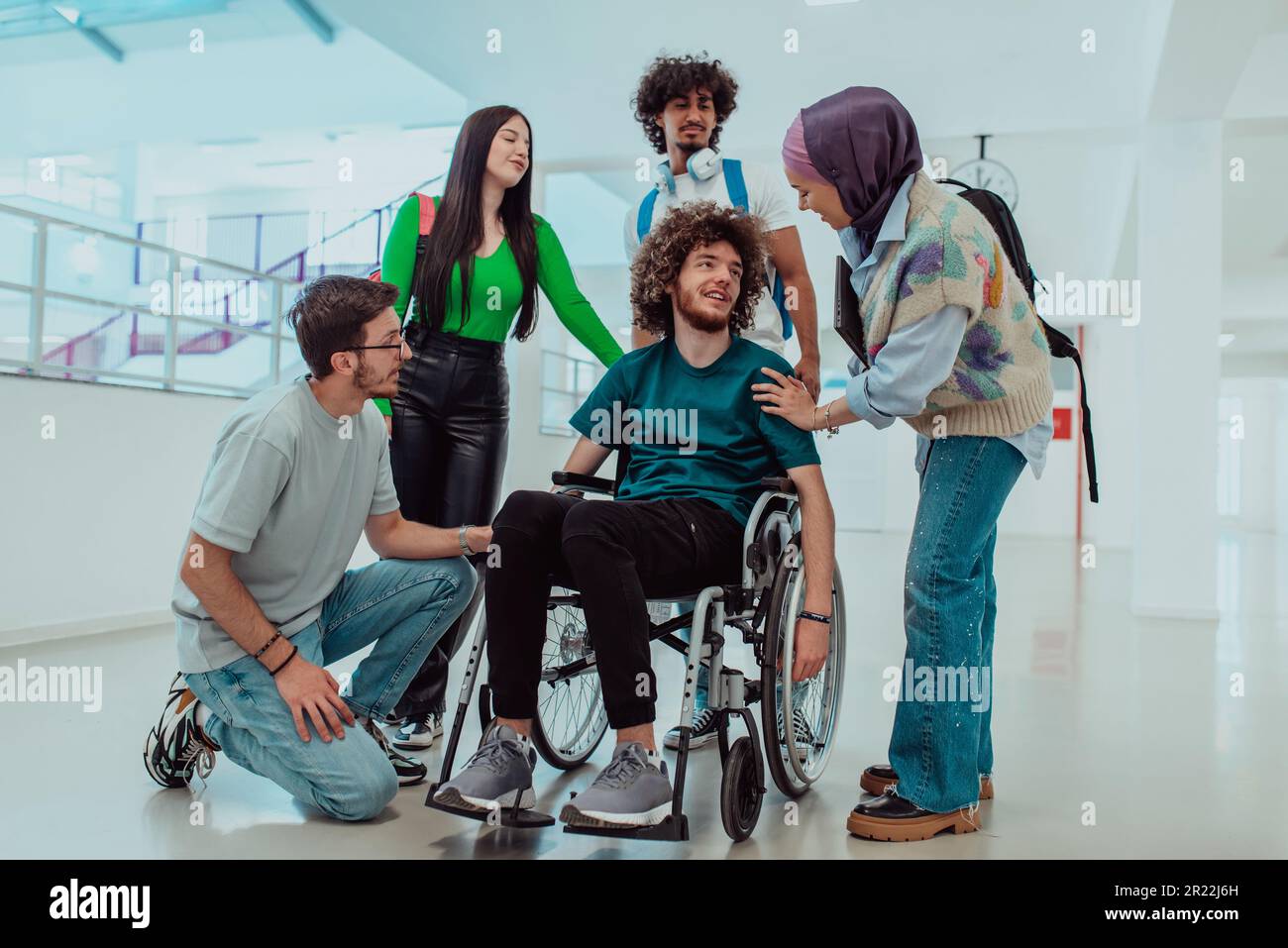 Un gruppo diversificato di studenti, tra cui uno studente afro-americano e un musulmano che indossa un hijab, sostengono il loro amico con disabilità in una sedia a rotelle Foto Stock