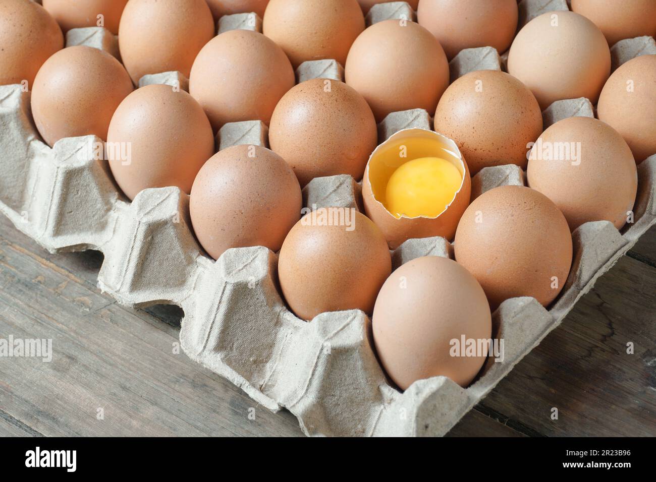 Uova di pollo in una scatola di cartone con metà uovo rotta con un tuorlo Foto Stock