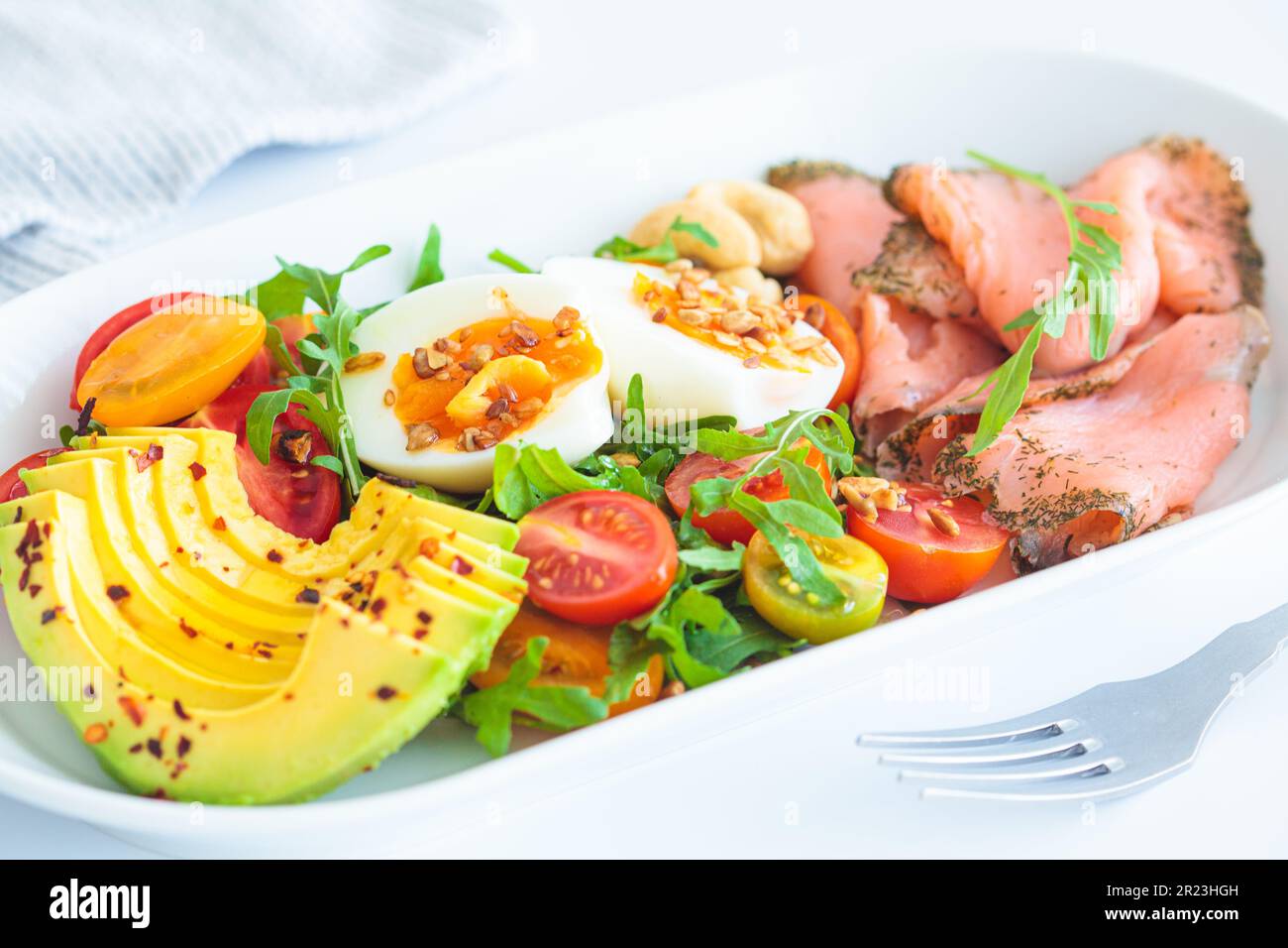 Colazione al keto con salmone, uova, avocado e noci su un piatto bianco, sfondo bianco, primo piano. Basso carb, dieta ad alto contenuto di grassi. Foto Stock