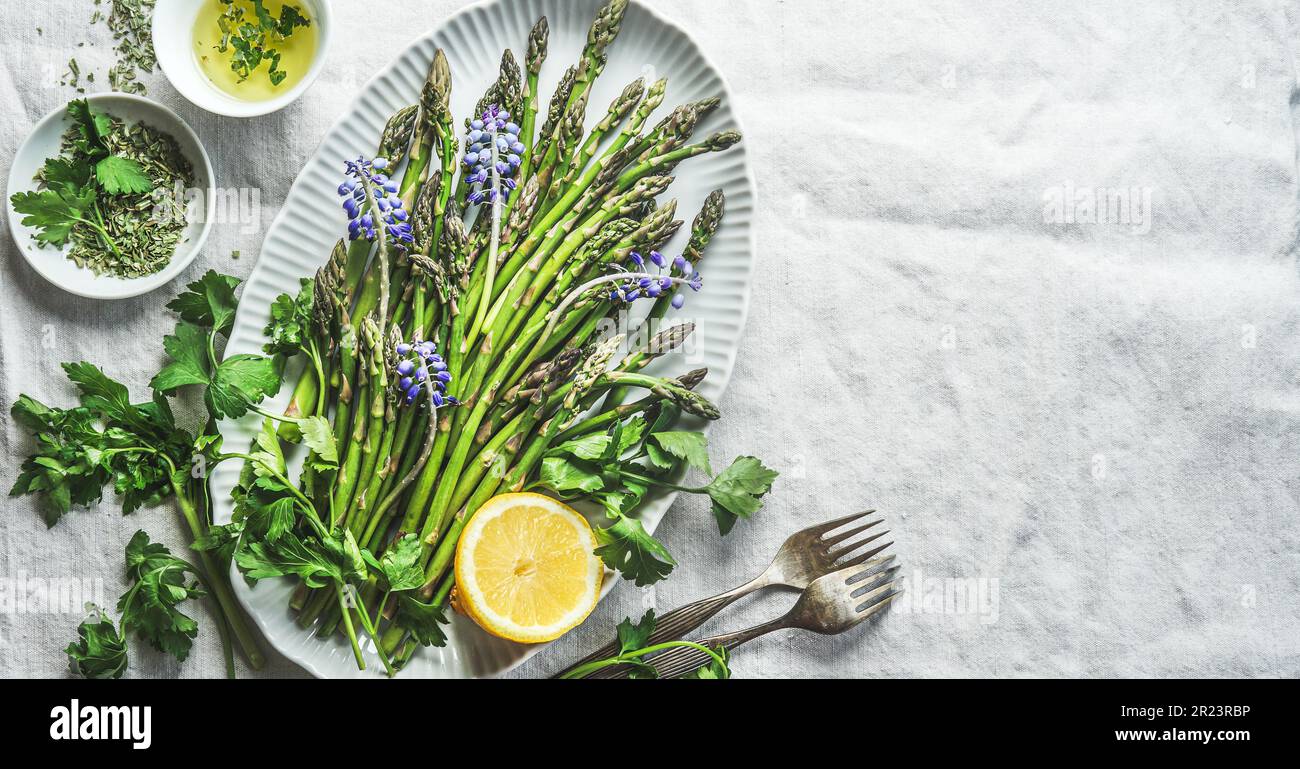Asparagi verdi su piatto con fiori, limone e ingredienti per gustosa cucina stagionale, vista dall'alto con spazio copia Foto Stock