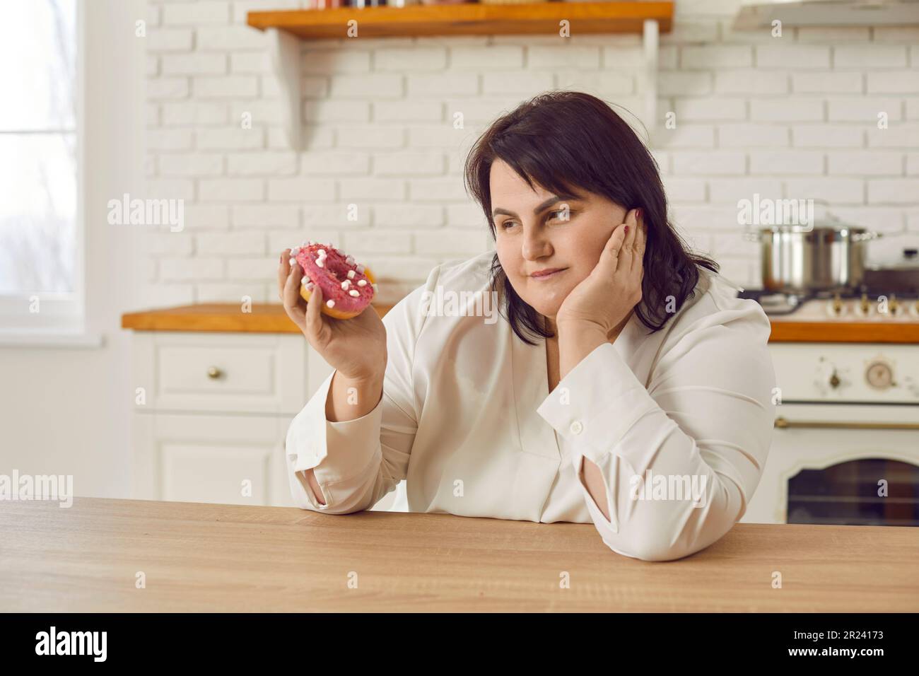 Giovane donna in sovrappeso penosa che esita a mangiare ciambella Foto Stock