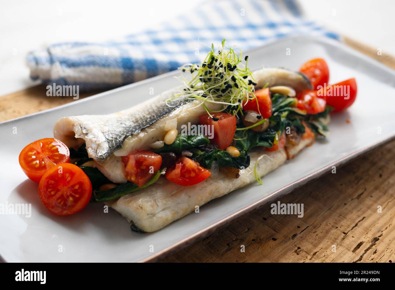 Filetto di spigola al forno ripieno di spinaci, pinoli e pomodori ciliegini. Foto Stock