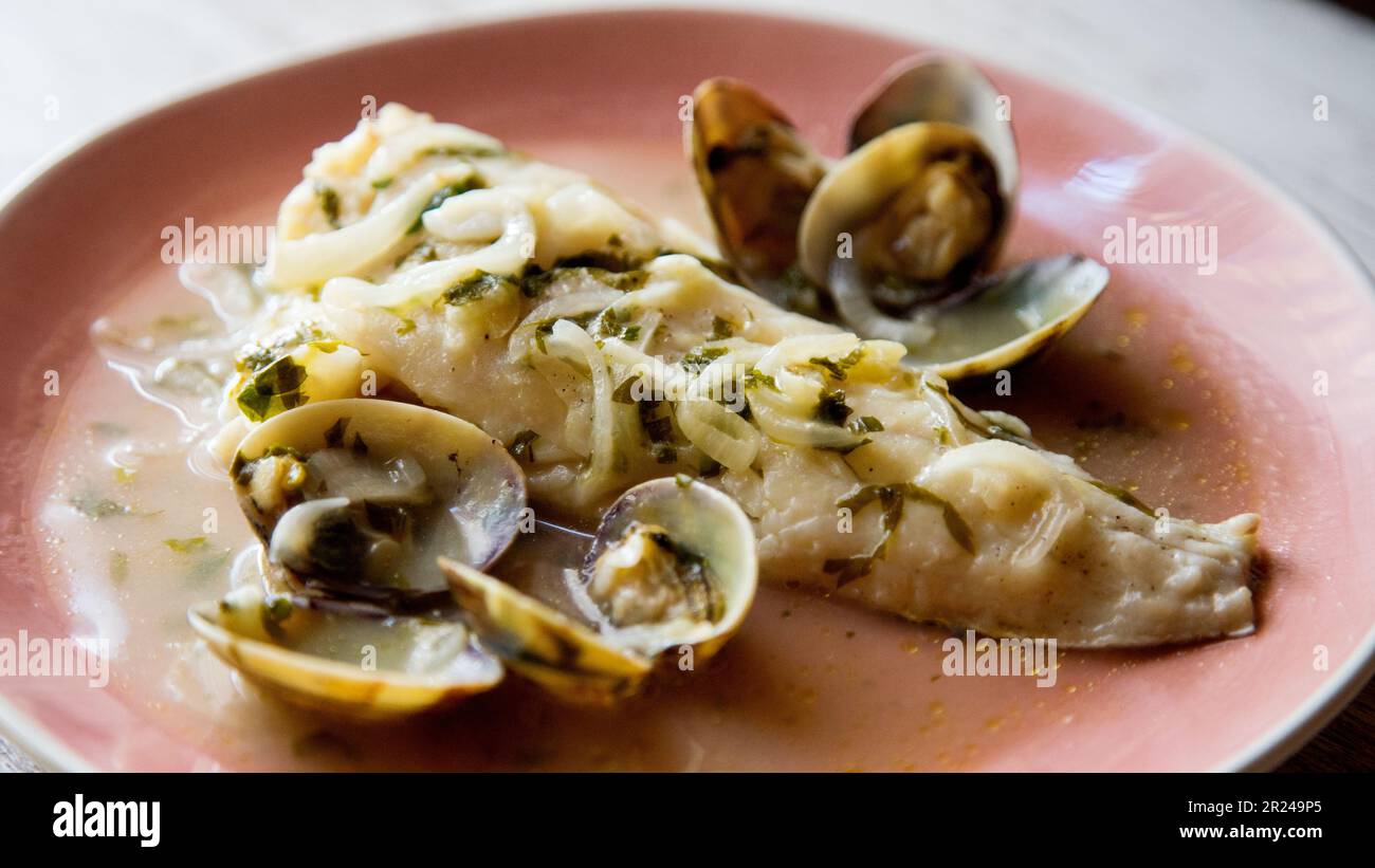 Nasello cotto con prezzemolo verde e salsa all'aglio servito con vongole. Ricetta spagnola tradizionale. Foto Stock