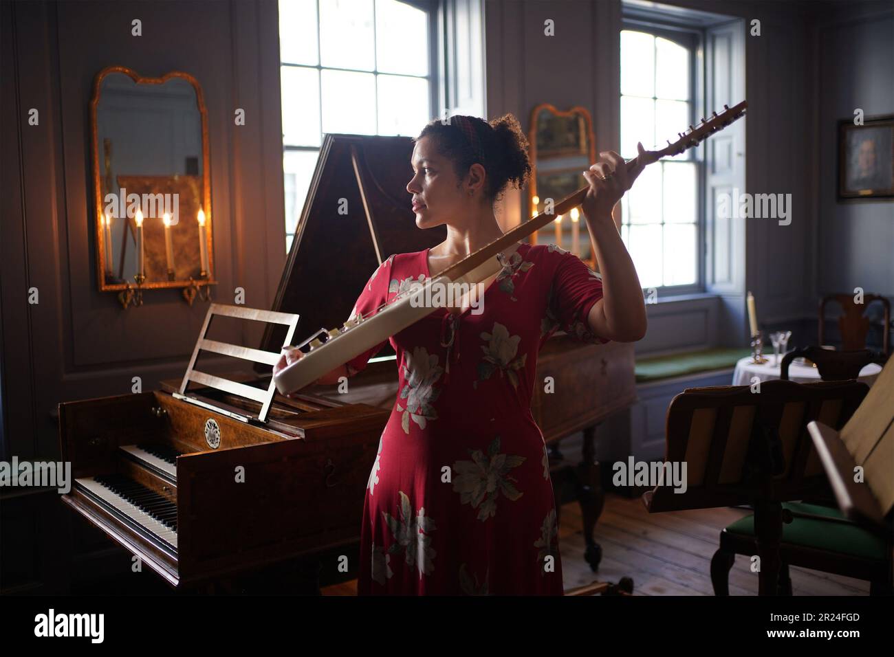 Il membro dello staff della Handel Hendrix House Rebecca Stephenson posa con una chitarra elettrica accanto a un clavicembalo nel salotto, durante un'anteprima delle nuove mostre su George Frideric Handel e Jimi Hendrix presso il museo Handel Hendrix House di Londra. Il museo è in fase di riapertura a seguito del 3million progetto Hallelujah, che ha portato a termine il restauro della casa londinese di Handel, dove visse 300 anni fa. Data immagine: Mercoledì 17 maggio 2023. Foto Stock