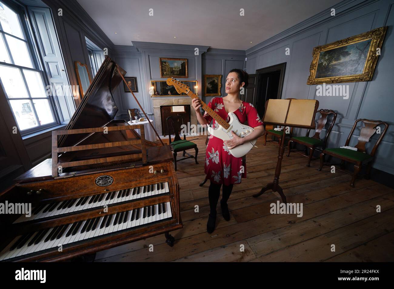 Il membro dello staff della Handel Hendrix House Rebecca Stephenson posa con una chitarra elettrica accanto a un clavicembalo nel salotto, durante un'anteprima delle nuove mostre su George Frideric Handel e Jimi Hendrix presso il museo Handel Hendrix House di Londra. Il museo è in fase di riapertura a seguito del 3million progetto Hallelujah, che ha portato a termine il restauro della casa londinese di Handel, dove visse 300 anni fa. Data immagine: Mercoledì 17 maggio 2023. Foto Stock