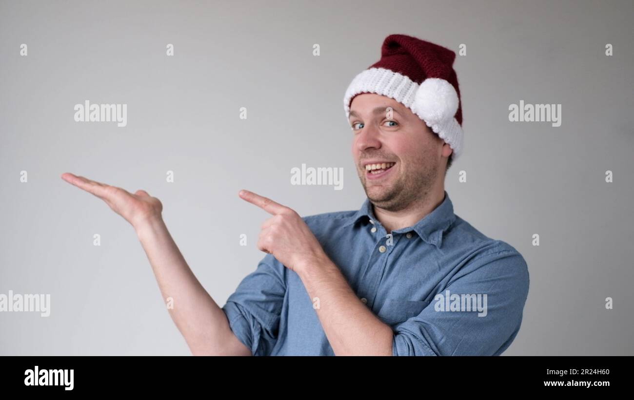 Il gioioso giovane europeo in un cappello di Capodanno indica uno spazio vuoto, presentando un prodotto Foto Stock