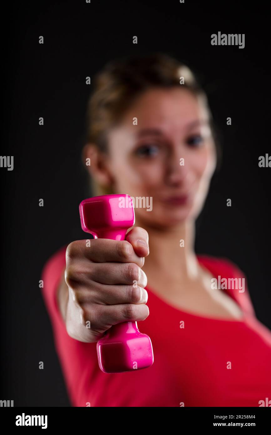 Donna fitness sollevamento peso rosa, sfocato sullo sfondo. Orgoglioso biondo, top rosso, che mostra gli obiettivi raggiunti. A stomaco piatto, uomo sana in corpi sano - i Foto Stock