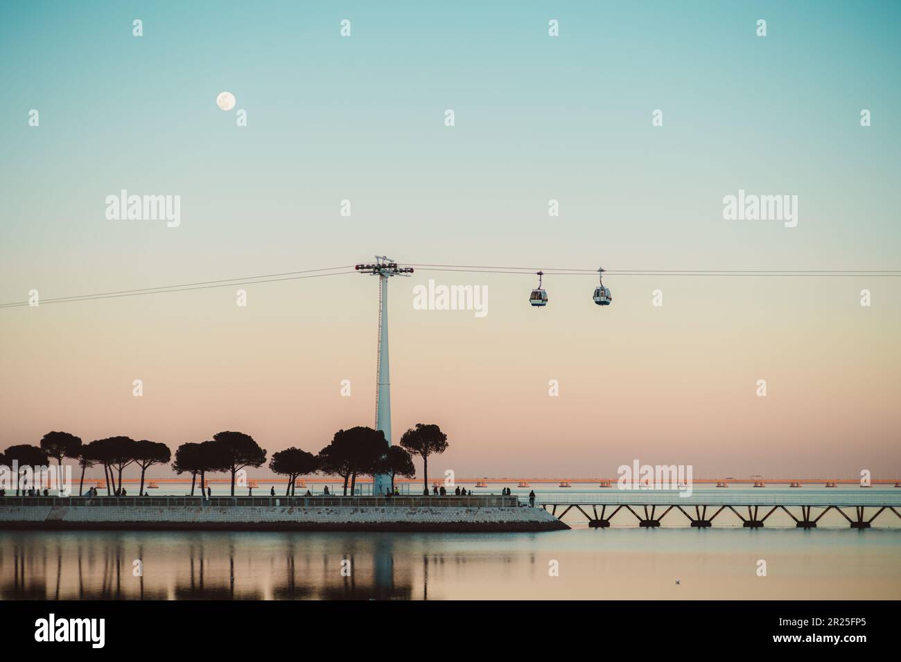 Lisbona; una splendida scena al tramonto dal basso, caratterizzata da una luna piena, un tramonto dal cielo rosa, il fiume Tejo e una funivia. L'effetto complessivo è un sereno e d Foto Stock