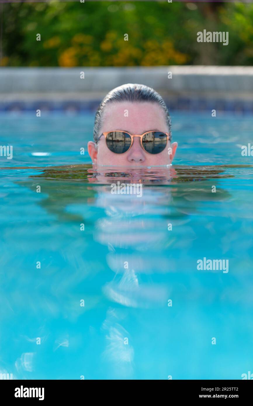 Signora in piscina. , capelli leccati, acqua fino alla bocca indossando occhiali da sole. Foto Stock