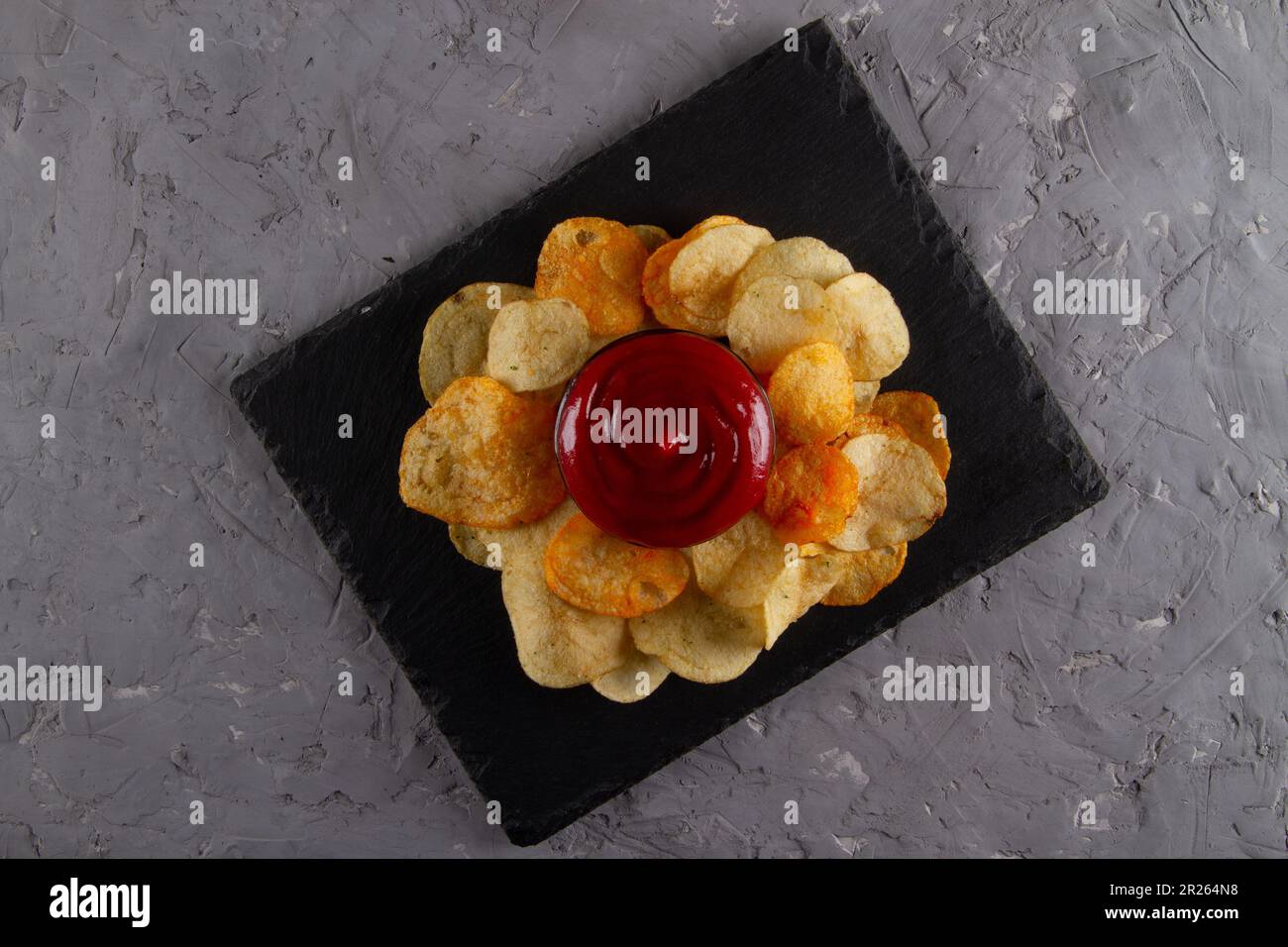 Vista dall'alto di un mucchio di patatine fritte con salsa di immersione rossa sul piano di servizio in ardesia nera sul tavolo in gesso grigio. Elegante e divertente piatto Foto Stock