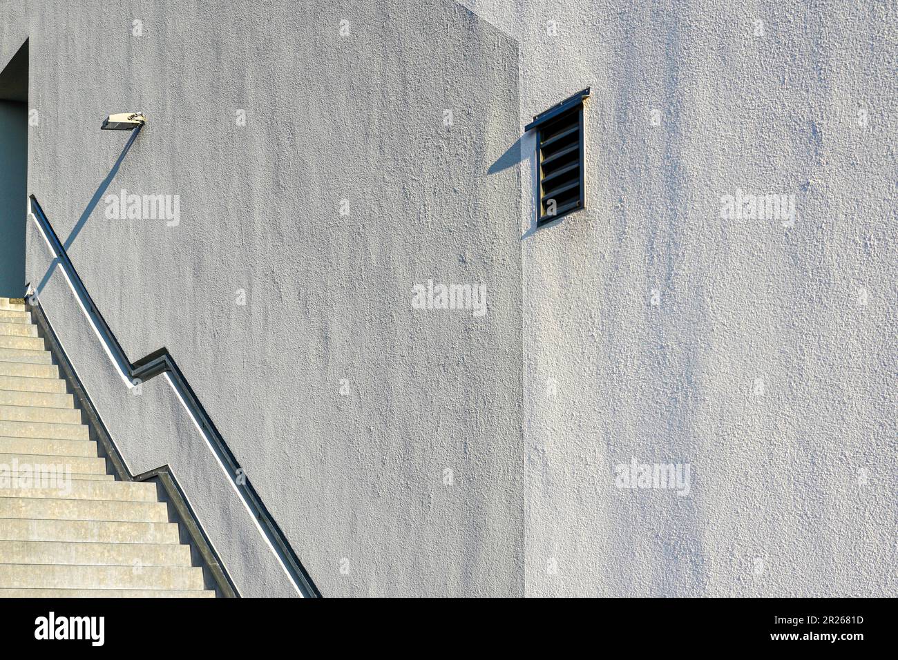 Una grande parete bianca sulla sinistra una scala metallica che conduce ad una porta alla luce del sole. Foto Stock