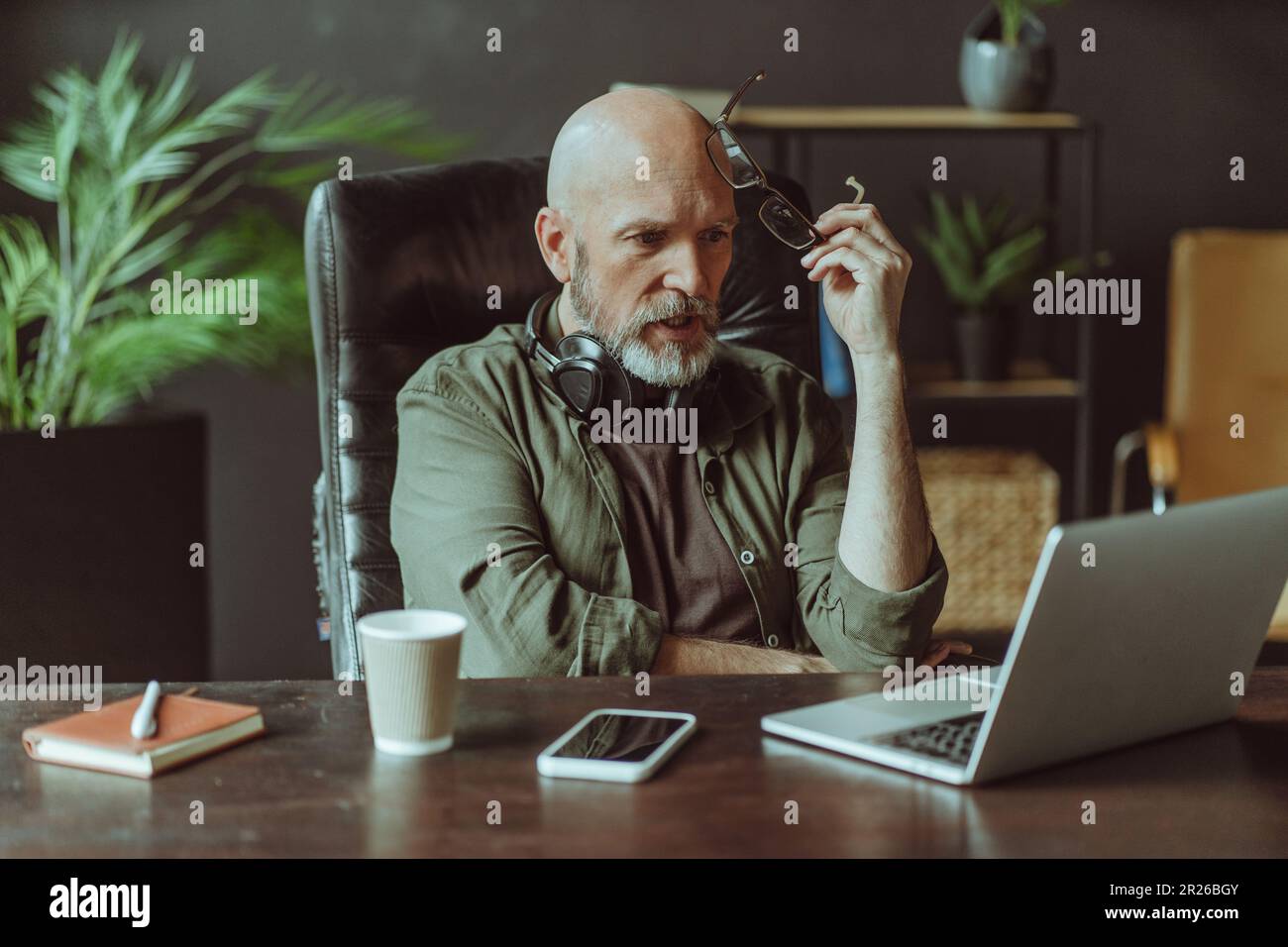 Scioccato uomo anziano maturo ha catturato la lettura di notizie sul notebook. L'uomo, con la sua distinta barba argentata, in posa chiusa mentre guarda intensamente lo schermo del computer mentre è seduto a casa. . Foto di alta qualità Foto Stock