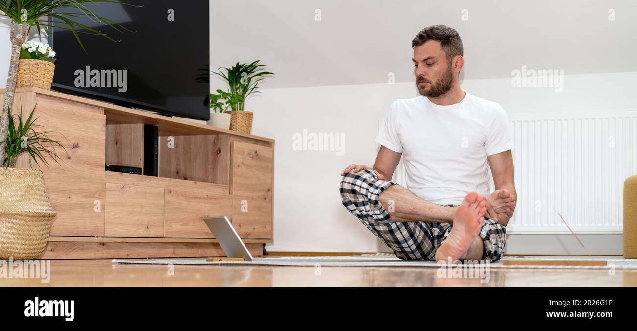 Uomo principiante imparare yoga esercizi per lo stretching online in internet utilizzando tablet. Foto Stock