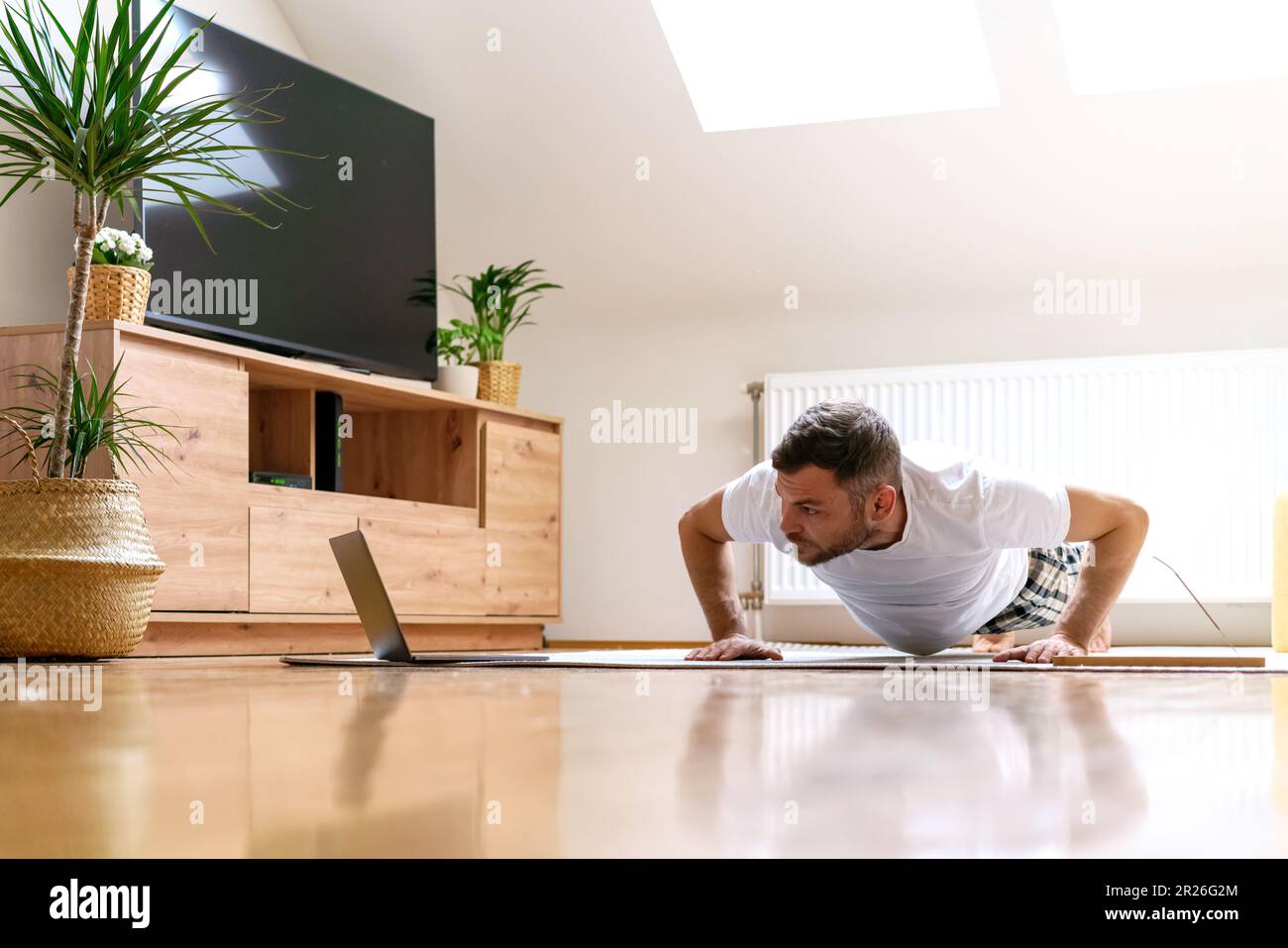 L'uomo che fa i push-up sul pavimento a casa, facendo l'asse, guardando l'allenamento online in Internet. Foto Stock