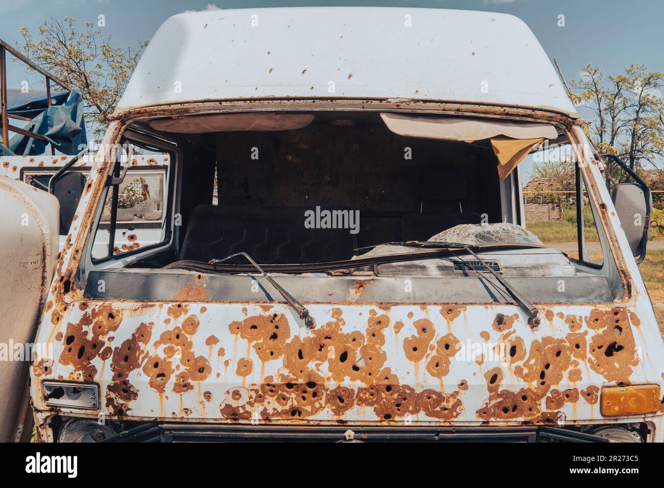 Cabina di un vecchio autobus (primo piano) danneggiato dal fuoco di artiglieria. Guerra in Ucraina. Invasione russa dell'Ucraina. Terrore della popolazione civile. Crimini di guerra Foto Stock