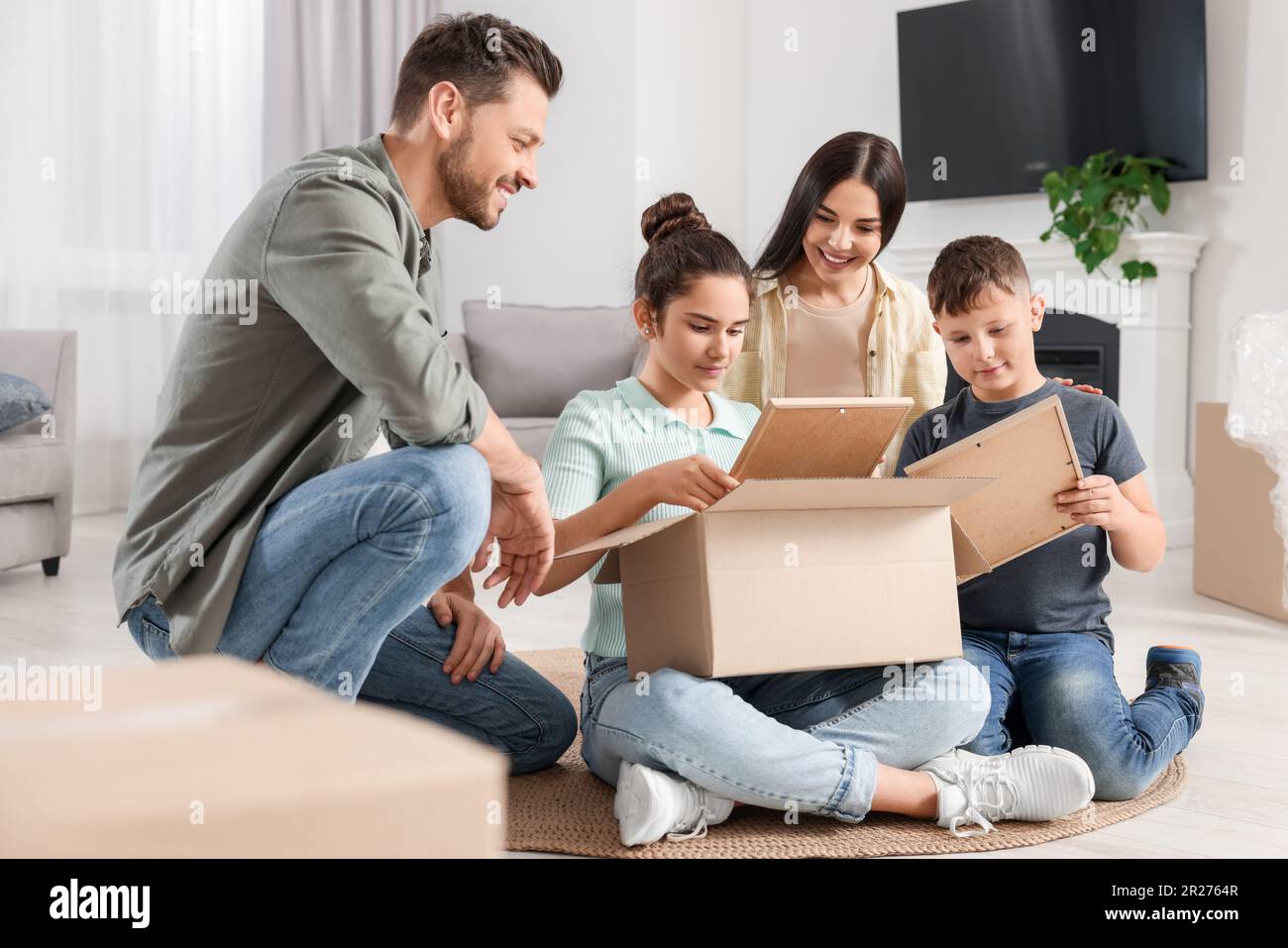 Felice famiglia che si insediano in nuova casa e disimballaggio scatole sul pavimento. Giorno in movimento Foto Stock