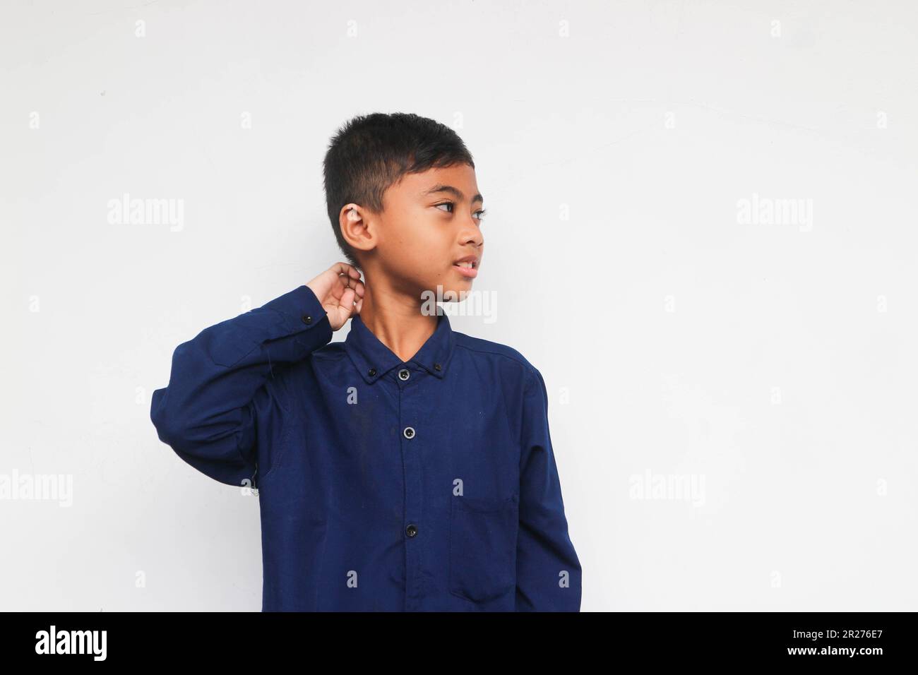 Carino ragazzo sconcertato in camicia blu guardando qualcosa con il sorriso isolato sullo sfondo bianco Foto Stock