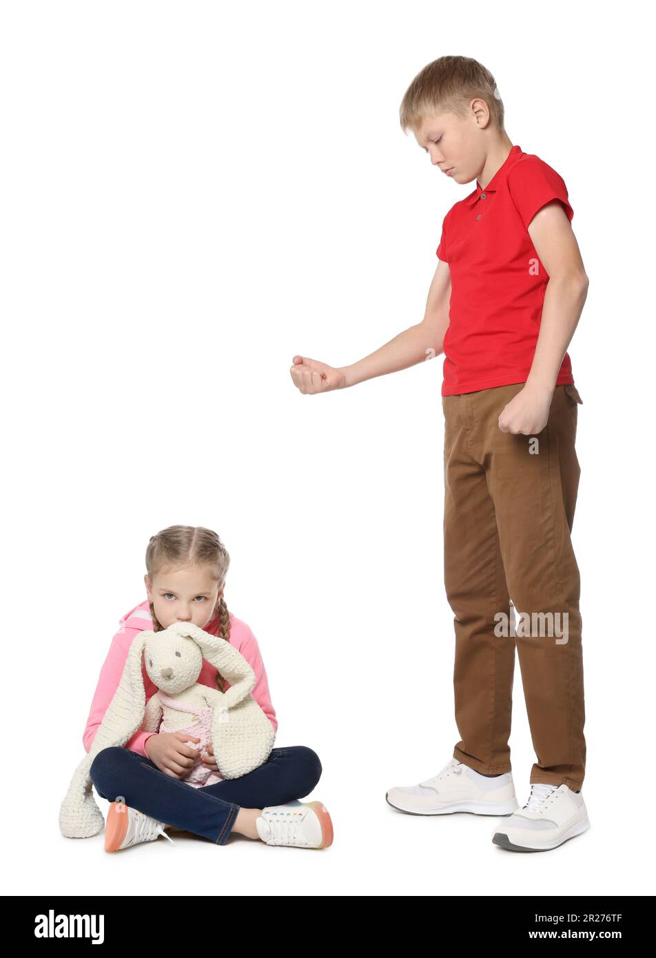 Ragazzo con pugno clenched guardando la ragazza spaventato su sfondo bianco. Bullismo dei bambini Foto Stock
