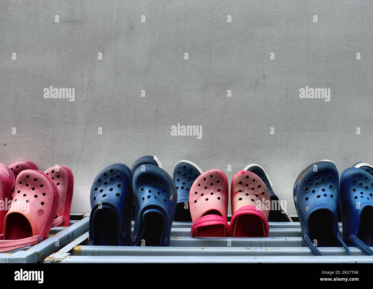 File di scarpe da spiaggia, barche e scarpe slip-on per il tempo libero del marchio Croc e Ditter in rosso e nero su una griglia metallica per l'aria e l'asciugatura al sole. Foto Stock