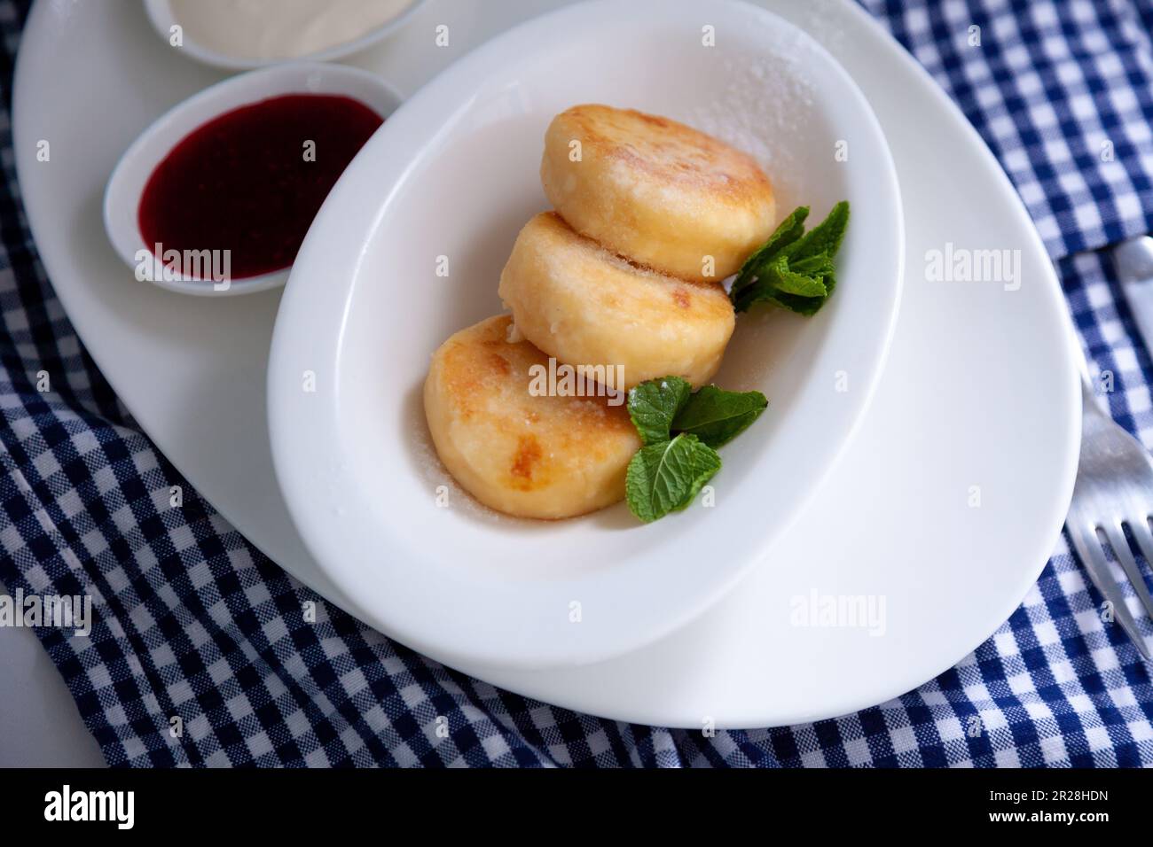 Frittelle di formaggio ricotta rotonda in un piatto bianco su sfondo blu. Cibo prima colazione. Cibo sano. Salsa di panna acida e menta. Primo piano vista dall'alto. Pasto dessert. Frittelle di ricotta al formaggio ricotta. Foto Stock
