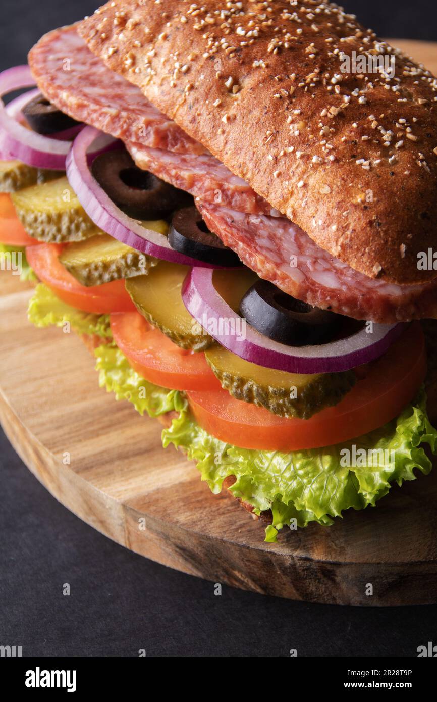 foto sandwich di salsiccia con cetriolo salato, pomodoro, lattuga, olive e cipolle su un asse di legno Foto Stock