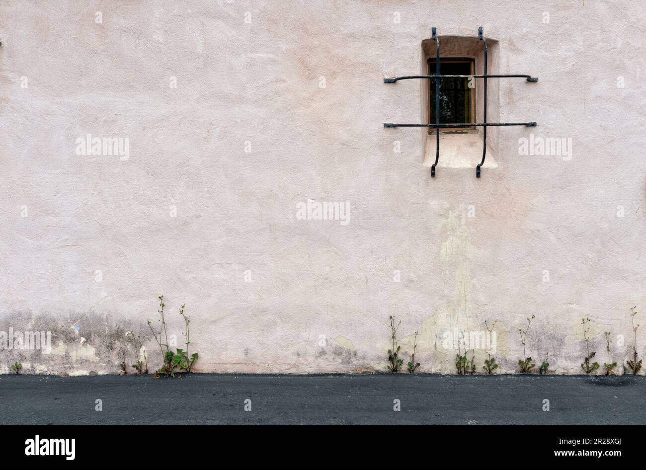 Vecchio muro stagionato con piccola finestra e un terreno con piante Foto Stock