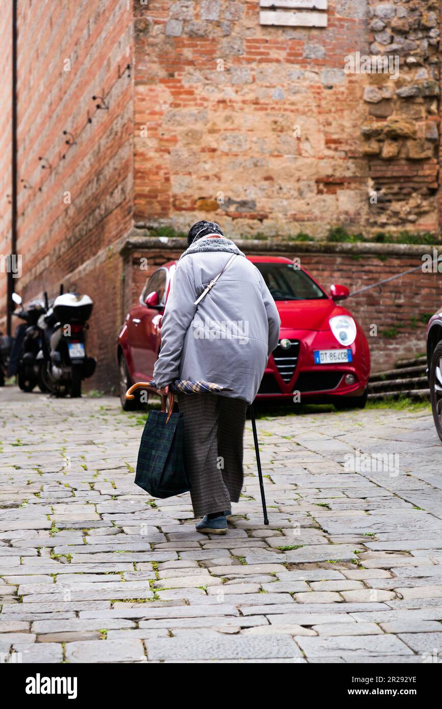 Siena, Italia - Apr 7, 2022: Donna anziana che cammina per le strade collinari di Siena, Toscana, Italia. Foto Stock