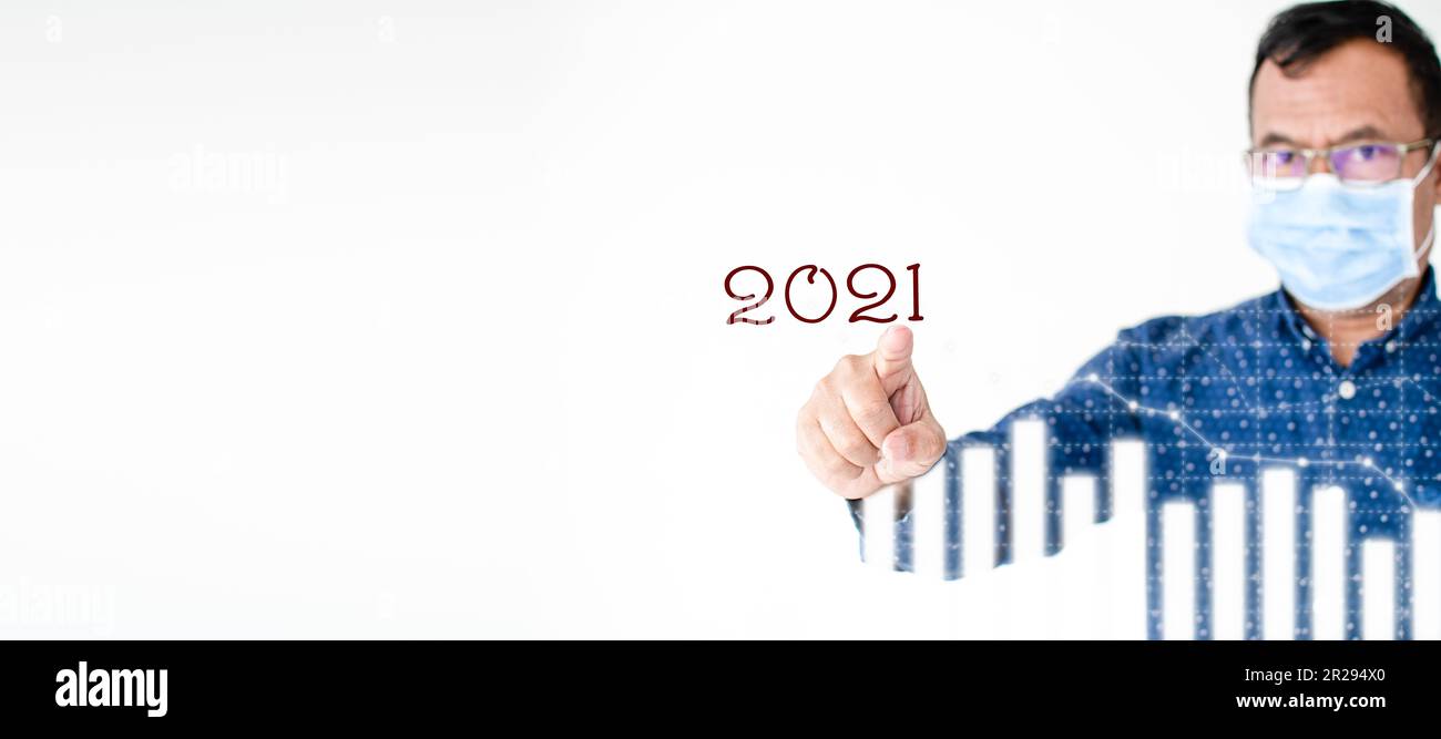 Primo piano, uomo d'affari che indossa una maschera di coronavirus, o COVID-19, sta puntando il dito su un grafico a colori che mostra l'attività di mercato 2021. Copia spazio su Foto Stock