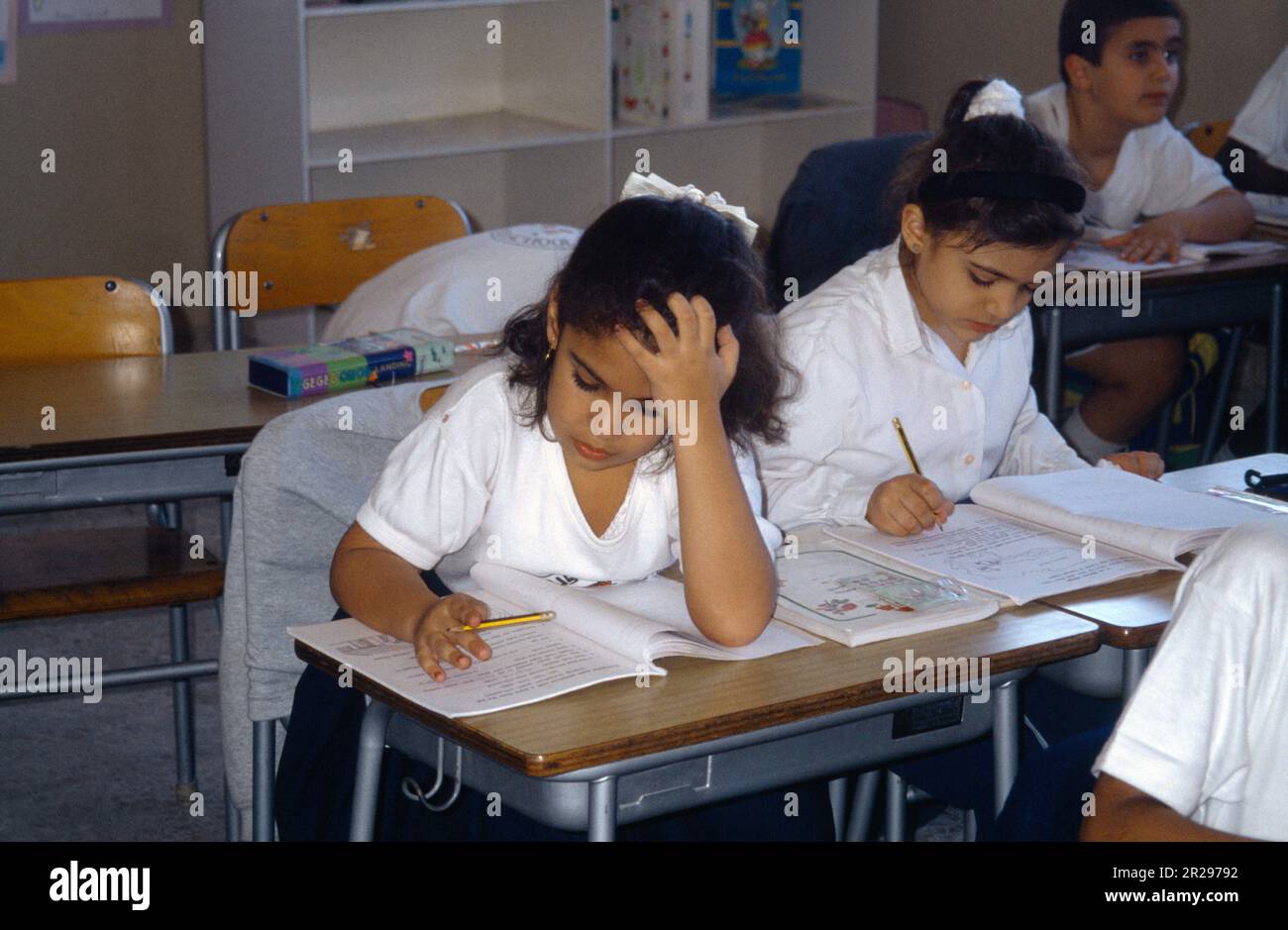 Abu Dhabi UAE Primary School Classroom Girl Writing con testa appoggiata alla scrivania Foto Stock