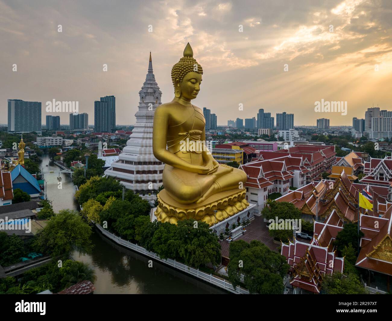 Una barca passava la statua del Grande Buddha (Phra Buddha Dhammakaya Thepmongkhon) nel tempio Wat Pak Nam Phasi Charoen situato vicino al fiume durante il tramonto. Foto Stock