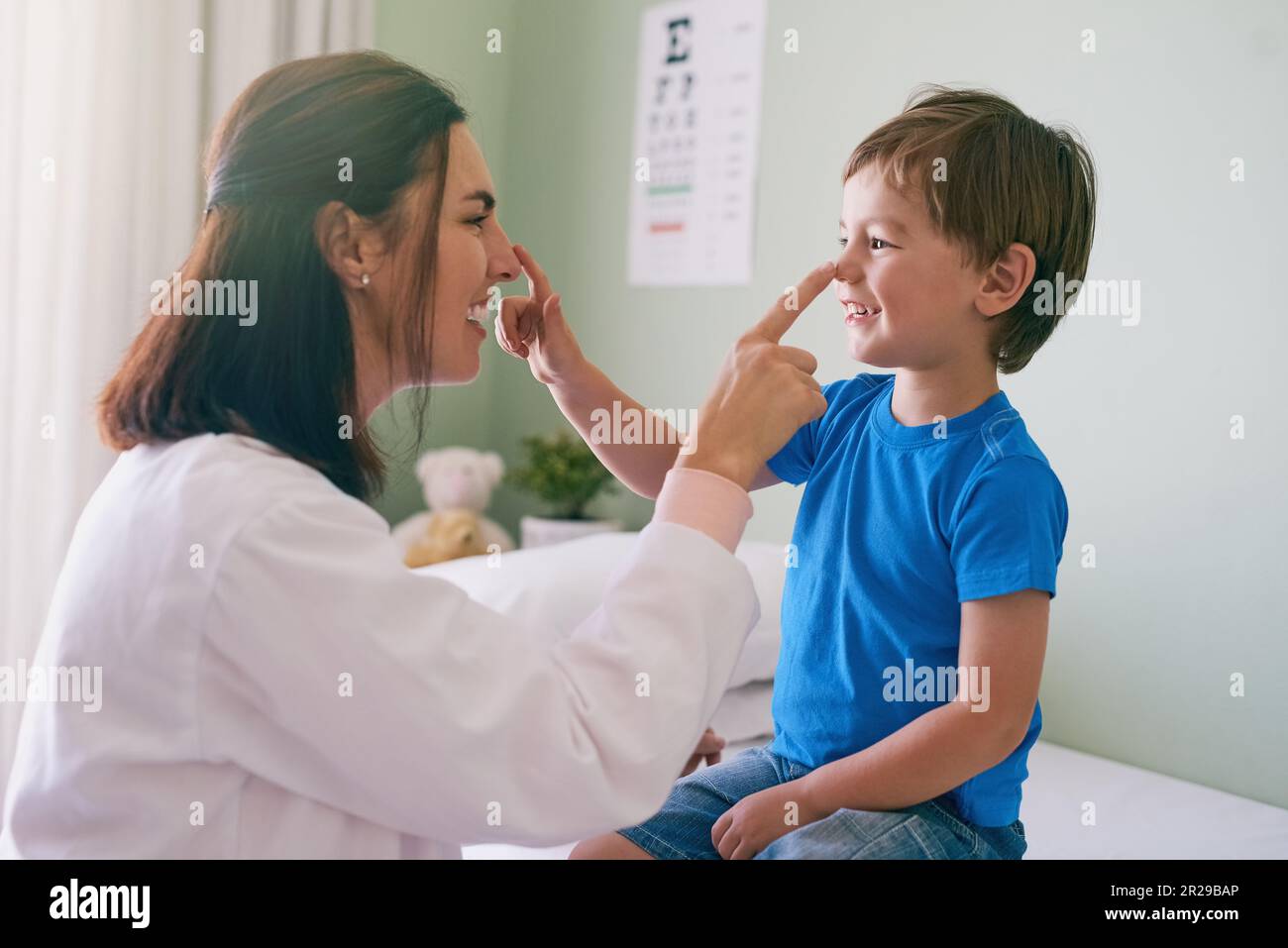 Donna medico, gioco e divertimento per bambini in un ospedale per la salute e la consultazione medica. Sorriso, fiducia e pediatra toccare il naso con una risata e. Foto Stock