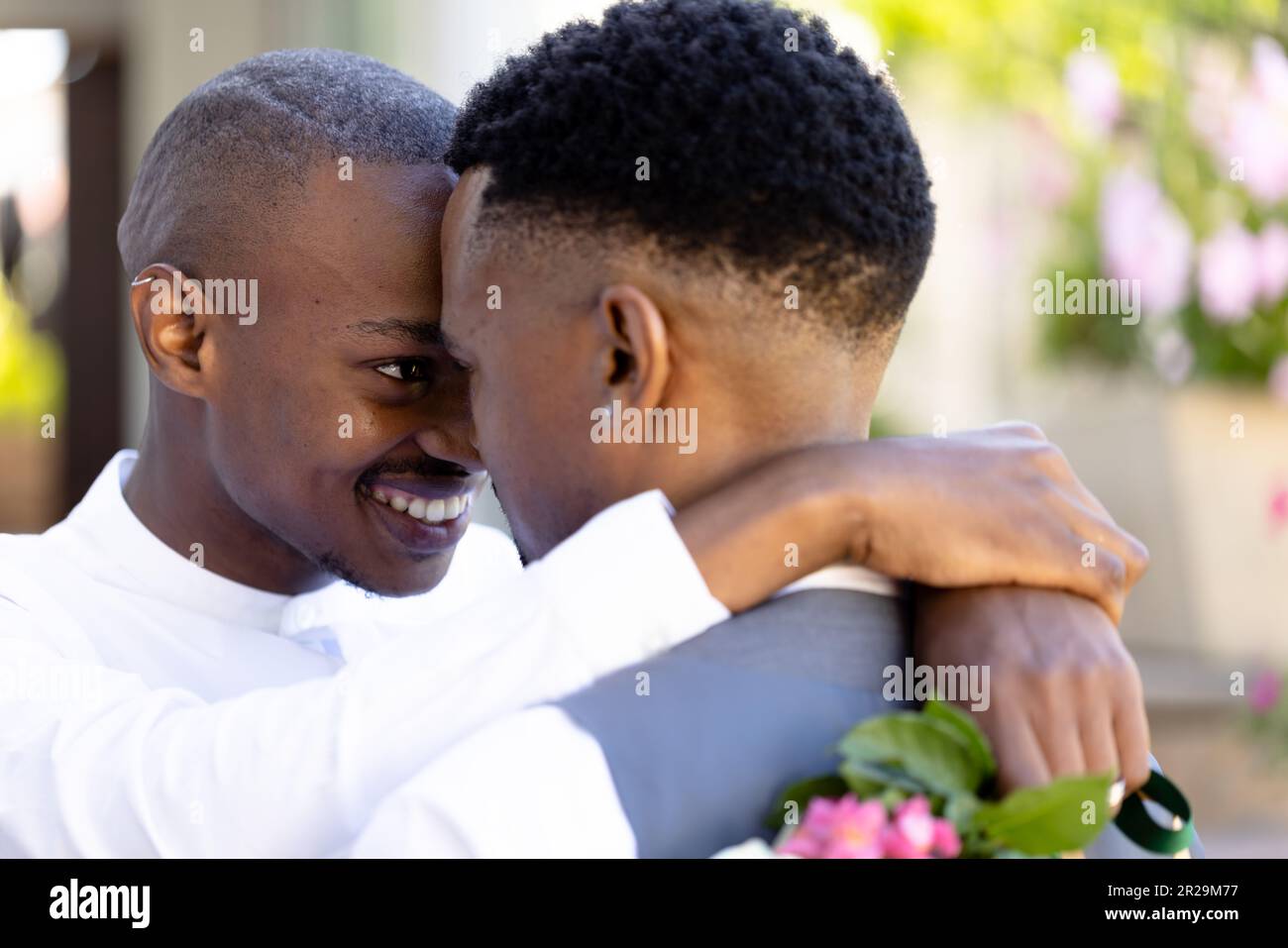 Primo piano di una coppia gay afro-americana con sposi faccia a faccia che abbraccia e posa alla cerimonia Foto Stock
