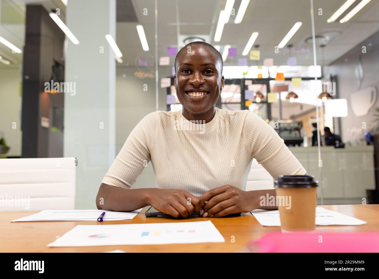 Ritratto di sorridente professionista afro-americana con relazioni sulla scrivania seduto in ufficio Foto Stock